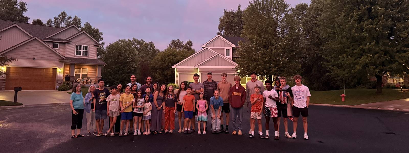 Neighbors gathered in the cul-de-sac under a pink evening sky